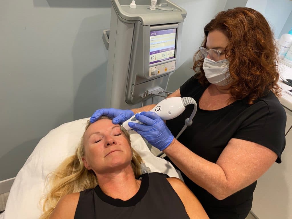 medical professional in blue gloves placing thermage skin tightening and contouring device on female patient's face