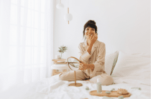 Happy woman in night suit sitting on bed and applying face cream.