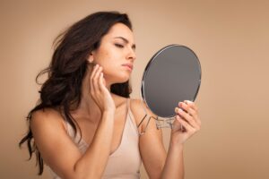 A woman looking in the mirror at acne on her face