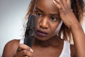 A woman with postpartum hair loss looking at hair in a comb
