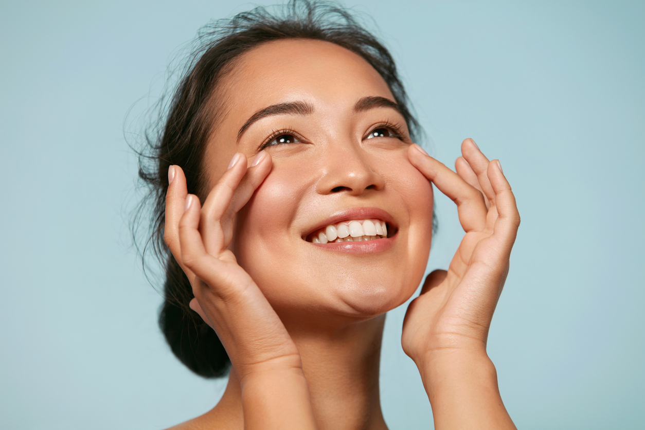 Smiling woman touching the skin beneath her eyes, representing smoother skin after SkinPen or Genius RF microneedling.