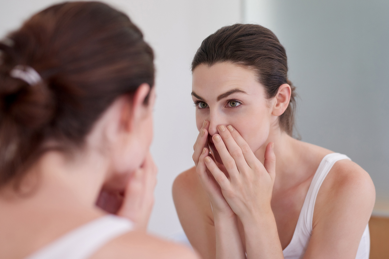 Woman examining the pores and texture around her nose while looking in a mirror.