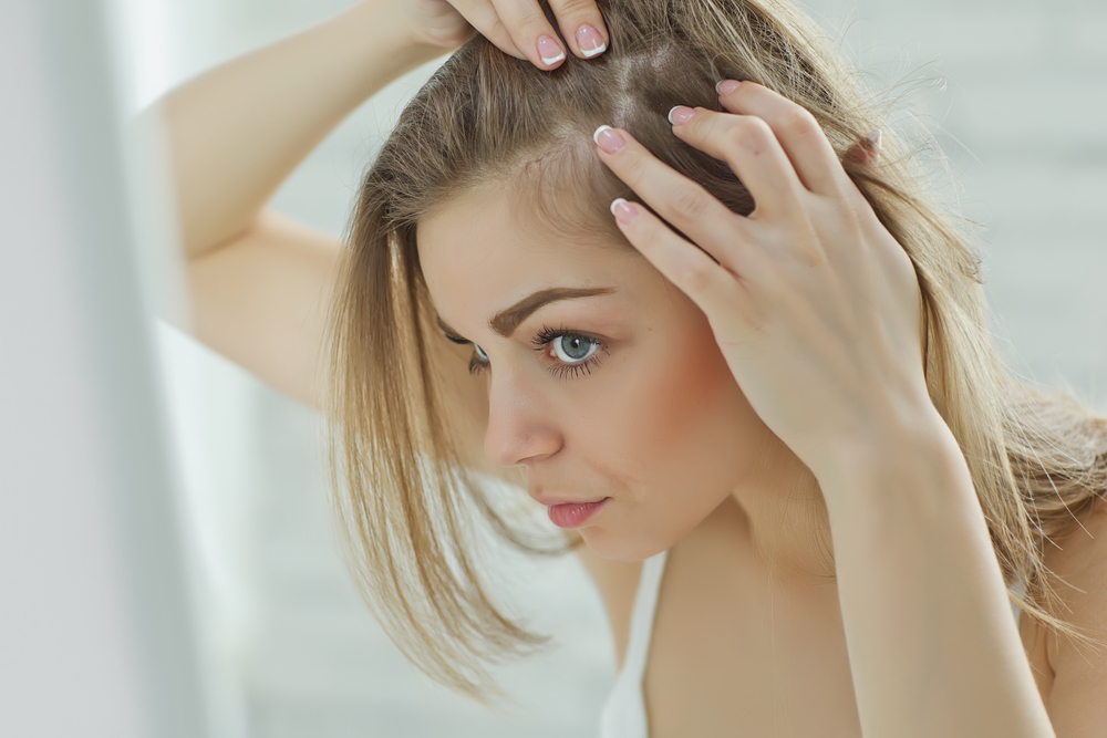 Woman examining early hair thinning near her temple in a mirror.