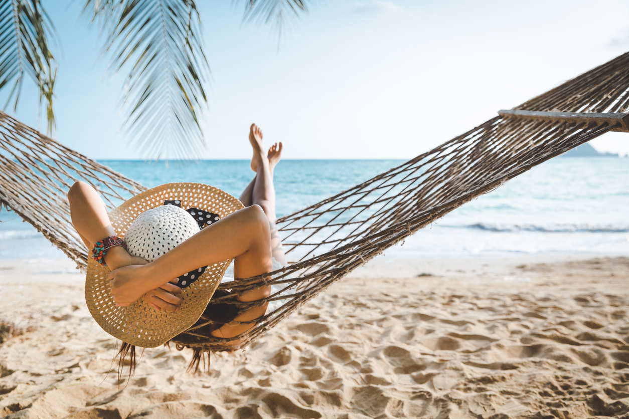 Woman relaxing in a hammock on a sunny beach, highlighting sun exposure considerations before laser hair removal.