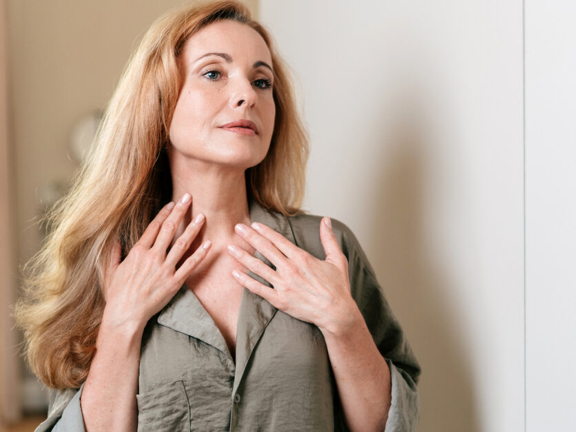 Woman examining the appearance of her neck in a mirror, representing visible signs of neck aging.